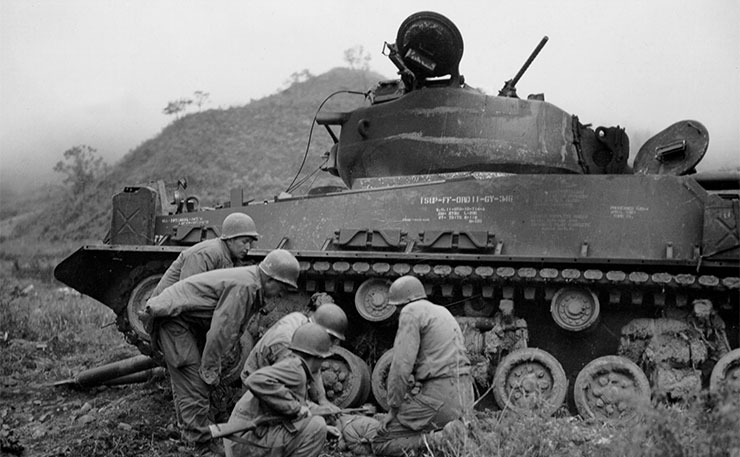 A demolition squad of Company A, 65th Engineer Battalion, 25th Infantry Division, place dynamite under the tracks of a burned out tank, under the supervision of the recovery platoon of C, 89th Tank Battalion, 25th Infantry Division. 14 Oct 1951.