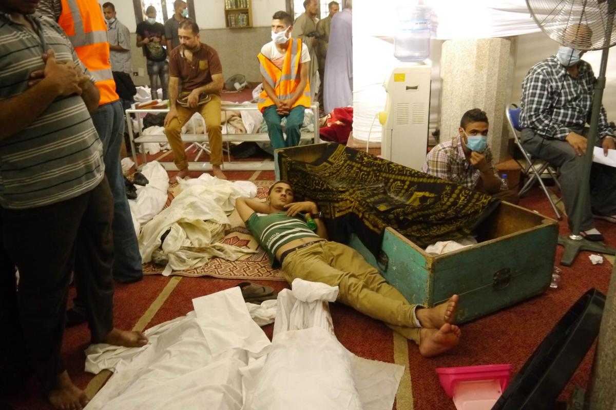 Al-Iman Mosque in Nasr City - top to bottom: (1) Corpses are lined up under melting blocks of ice, while attendants use fly spray, water atomisers full of disinfectant and incense to try and keep the the room fresh. (2) Attendants prepare to take an identified body to one of the private vans waiting outside to take it home. (3) A young man stares into space, lying on the soggy carpet among the bodies. Photos: Rachel Williamson